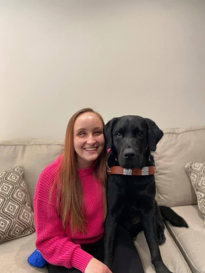 Founder, Zhenya Pankova, sits on a couch with Kingston, her black lab guide dog.