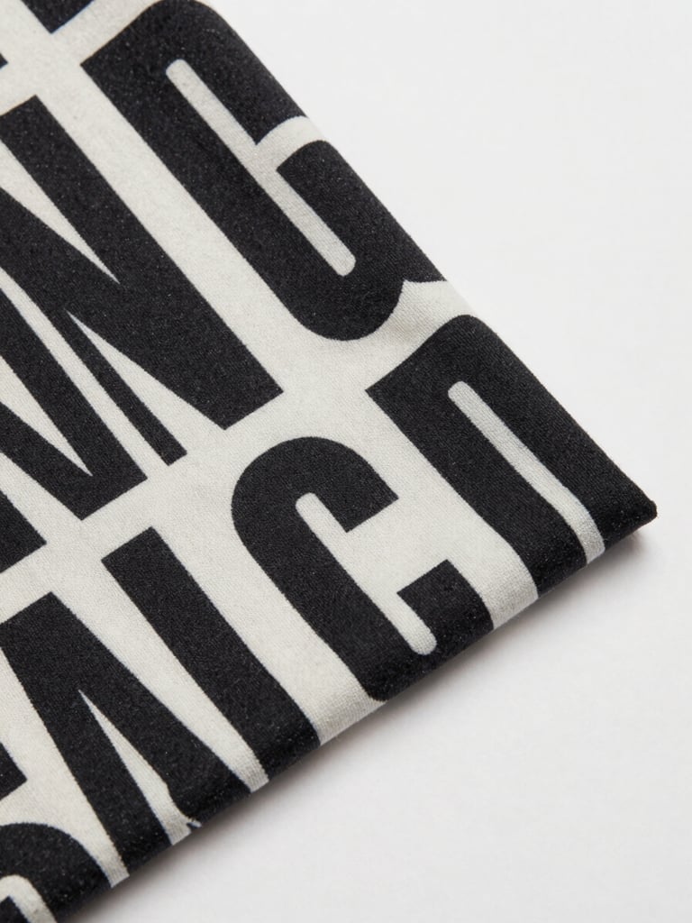 Overhead flat-lay of a custom-designed T-shirt on a clean off-white surface, bold graphic print visible, crisp studio strobe lighting, fabric texture sharp in frame, no props or distractions