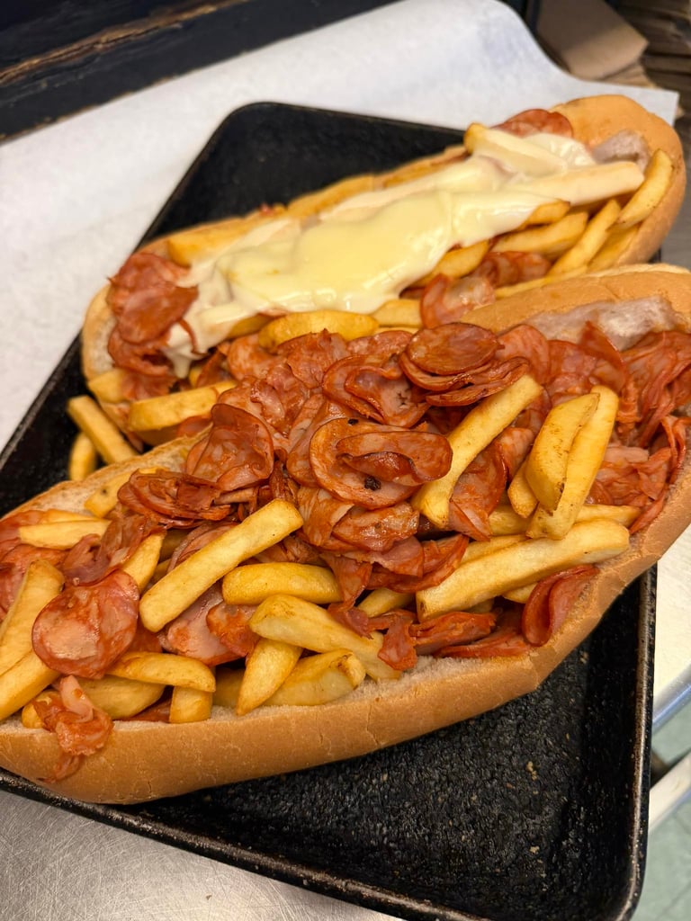 Two loaded submarine sandwiches topped with crispy french fries, sliced pepperoni, and melted cheese sauce.