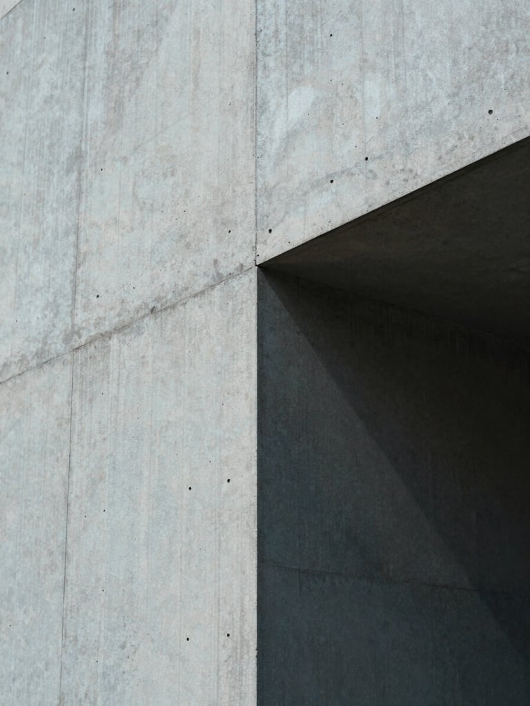 Macro crop of architectural concrete wall with sharp geometric shadows cast by cool indirect daylight, emphasizing spatial structure.