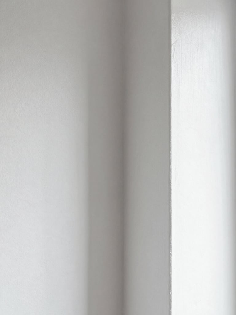 Extreme close-up panoramic of a painted interior wall corner junction, crisp 90-degree angle with zero paint bleed, matte white finish, natural window sidelight revealing texture uniformity, no people, clinical documentary proof shot