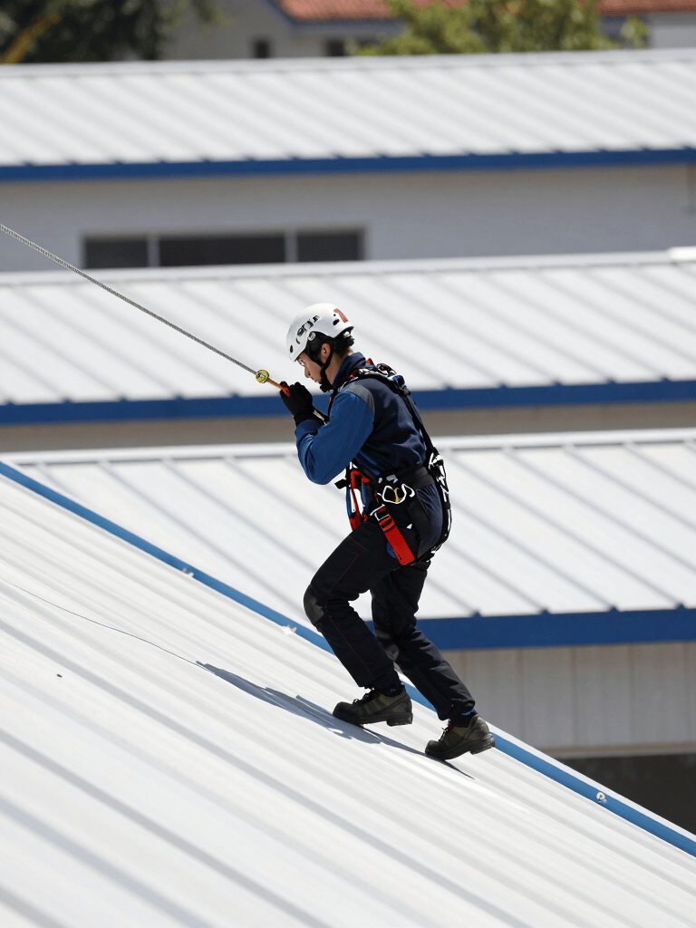 This professional is secured to a safety harness on a stainless steel lifeline cable on a white incl