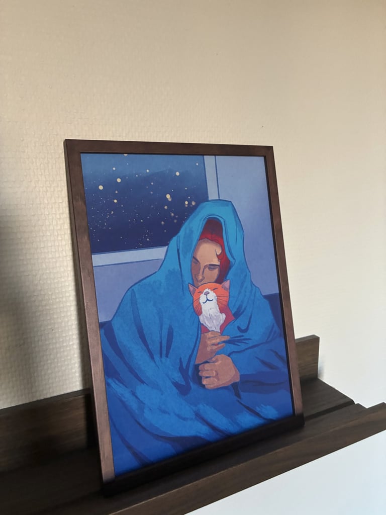 Framed painting of a woman and her orange cat snuggled under a blue blanket at night.