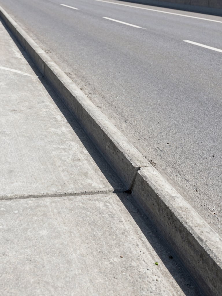 Close-up wide shot of a reinforced concrete expansion joint on a completed highway bridge deck, bright midday daylight, sharp structural detail visible across the full horizontal frame, neutral grey concrete texture, no workers, no equipment