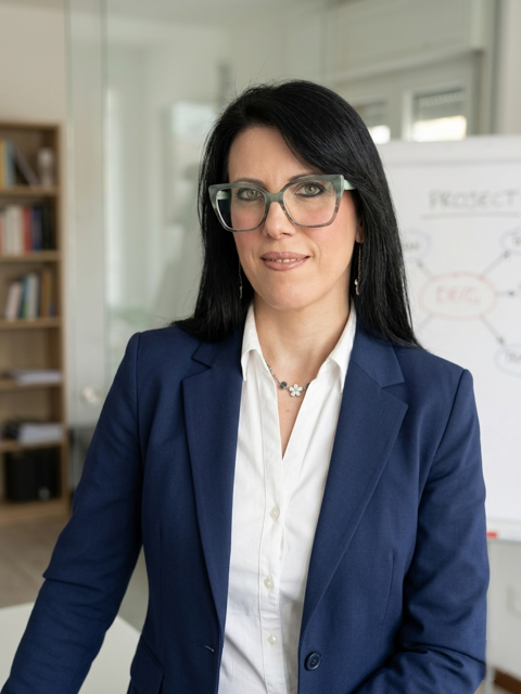 Professional businesswoman in a blue blazer and glasses standing in a bright office.