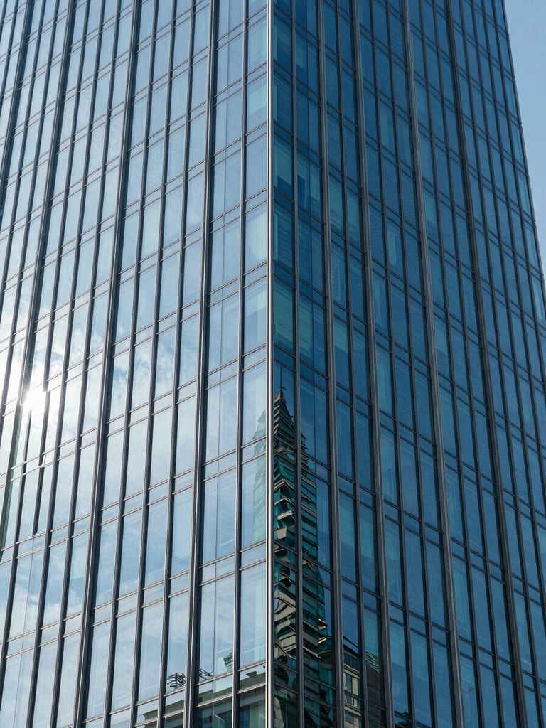Close-up architectural detail of a modern glass skyscraper facade reflecting the blue sky, clean geometric lines.