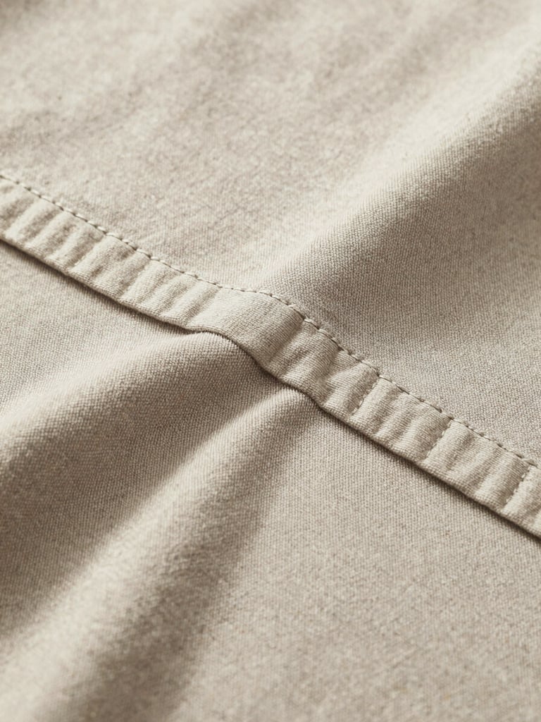 Extreme close-up of clean-finished interior seams on a heavy neutral-toned cotton garment, soft shadows highlighting the stitching.