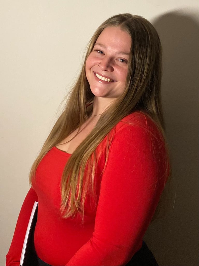 A smiling young woman with long blonde hair wearing a vibrant red top posing for a professional headshot.