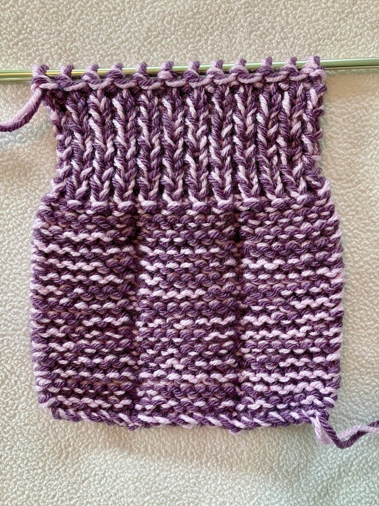 Flat knitted purple slipper on knitting needle, wrong side showing