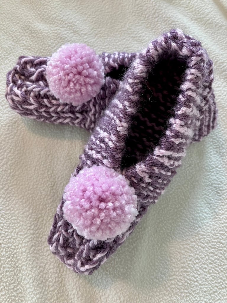 Pair of hand knitted purple slippers with light lavander pompoms