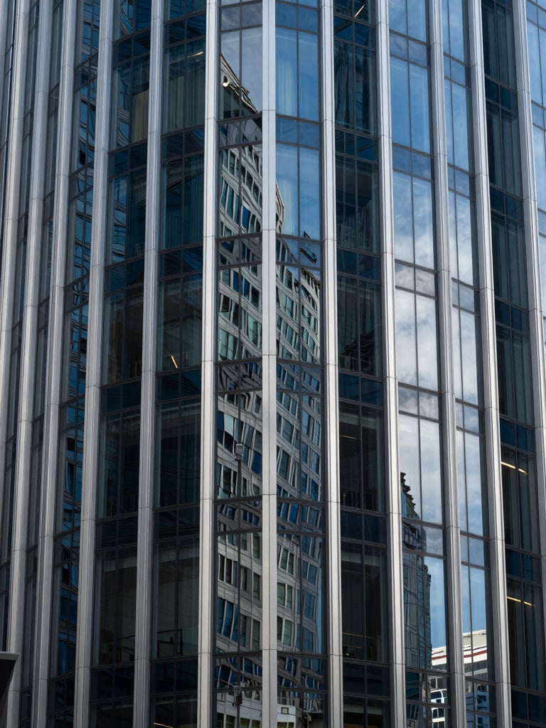 Crisp architectural crop of a modern financial district glass facade, sharp silver reflections and deep blue shadows, clean lines.