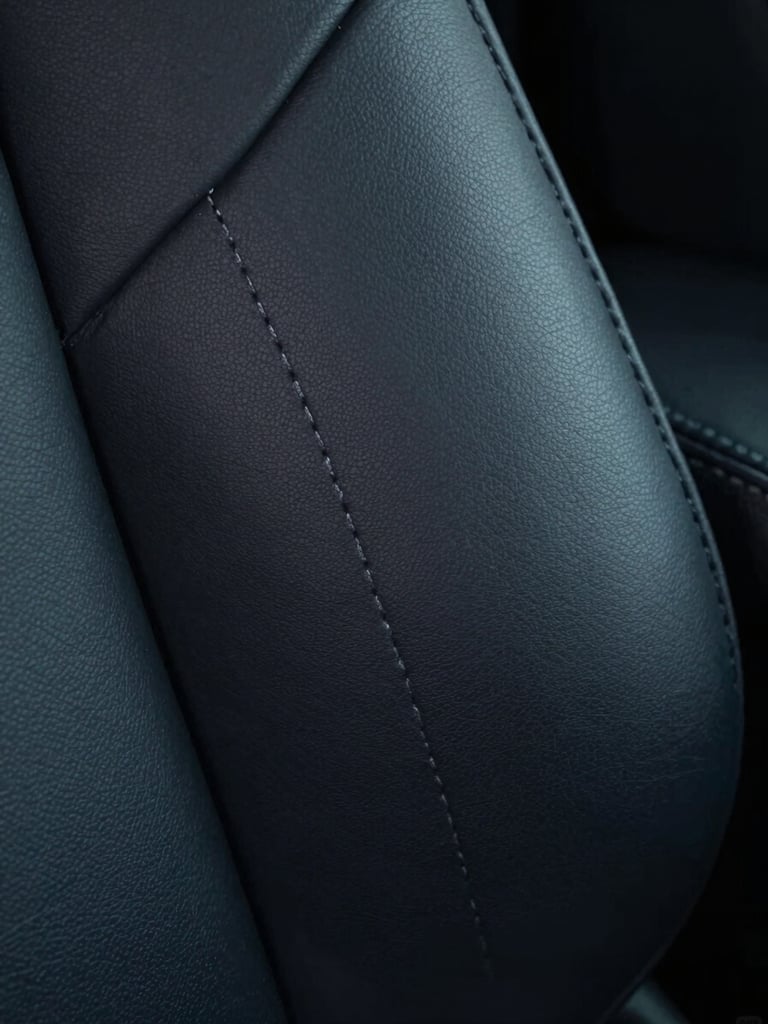 Macro shot of precise double stitching on a dark leather car seat, cool directional lighting highlighting the texture and zero dust.