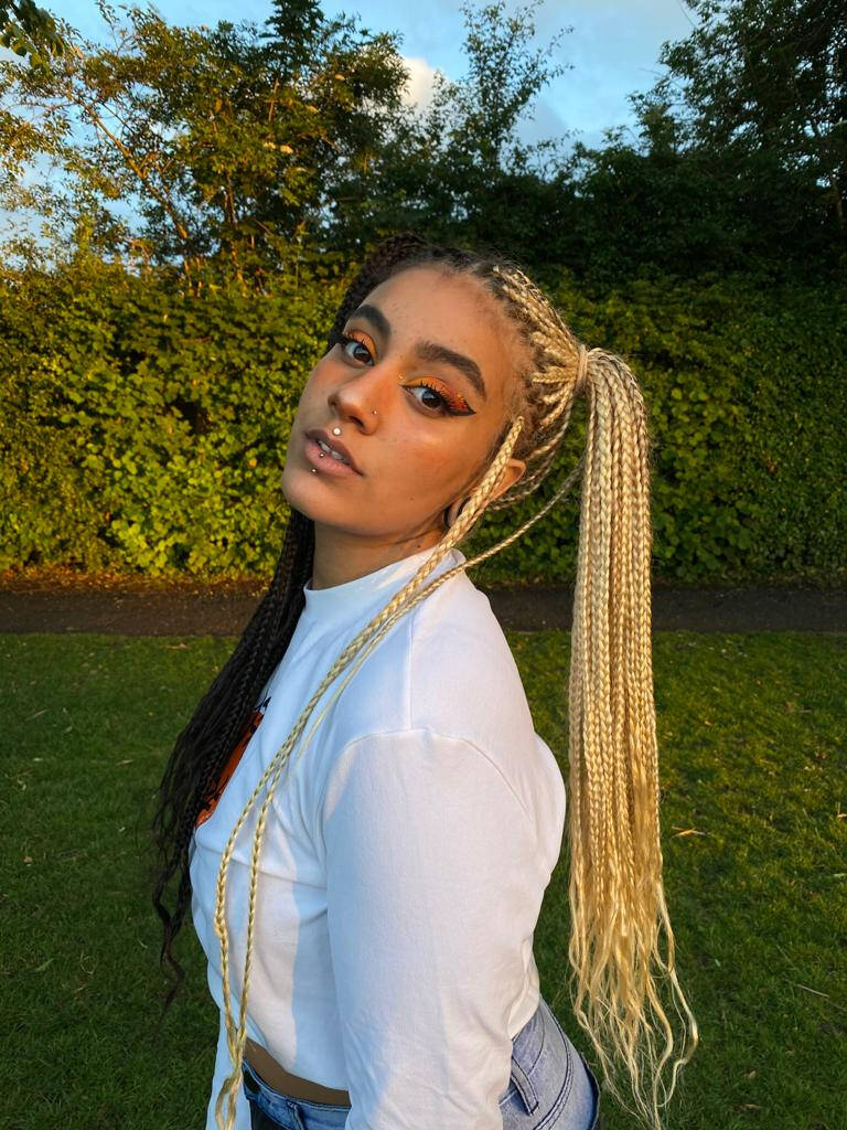 Woman with blonde and black split-dye box braids posing in a park at sunset.