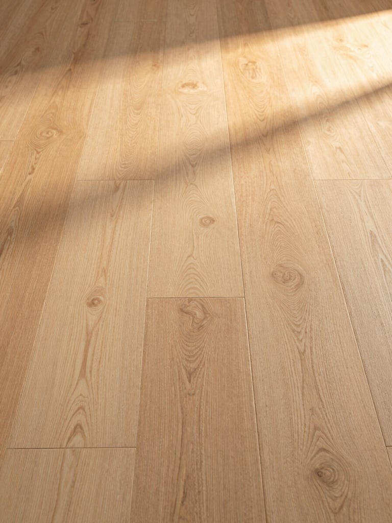 Wide close-up of freshly installed wide-plank white oak hardwood flooring filling the right frame edge to edge, warm golden-hour side light raking across the grain and seam lines, extreme horizontal framing, no people, no furniture