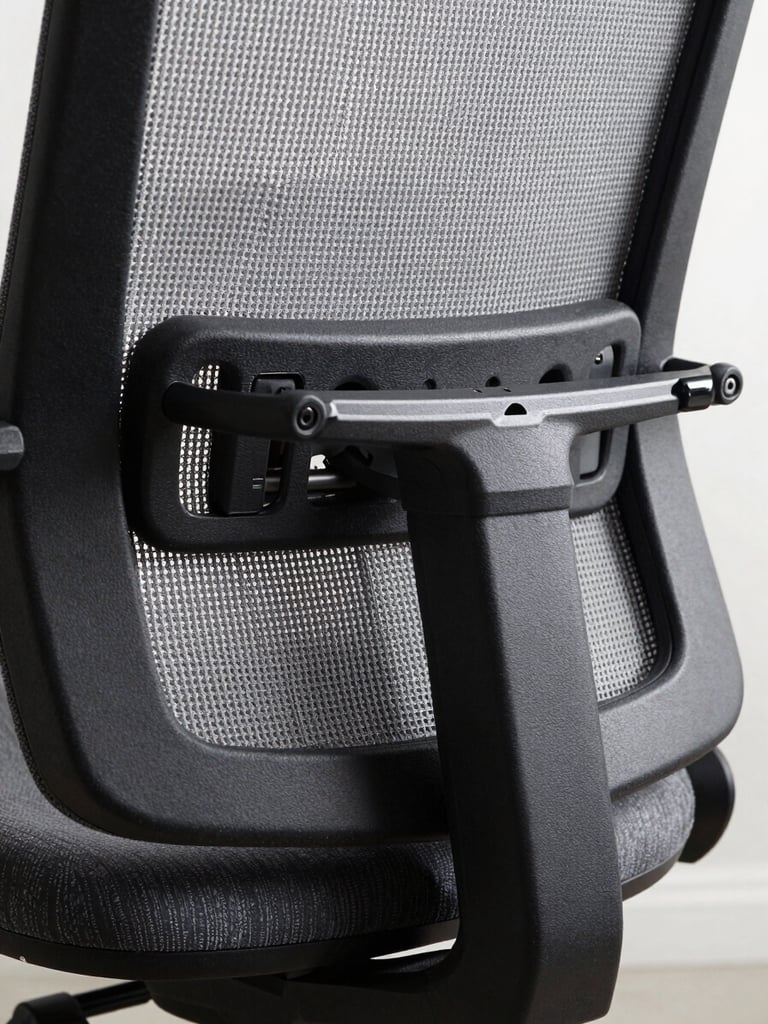 Extreme close-up of an ergonomic chair lumbar mechanism, grey mesh backrest and black polished adjustment lever, overexposed north-facing studio light emphasizing the precision engineering of the sliding lumbar support rail, no human presence