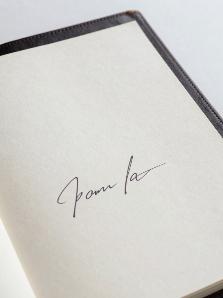 Close-up of a hand-signed certificate of provenance on heavy cotton paper, resting next to a leather-bound artist monograph, soft studio daylight