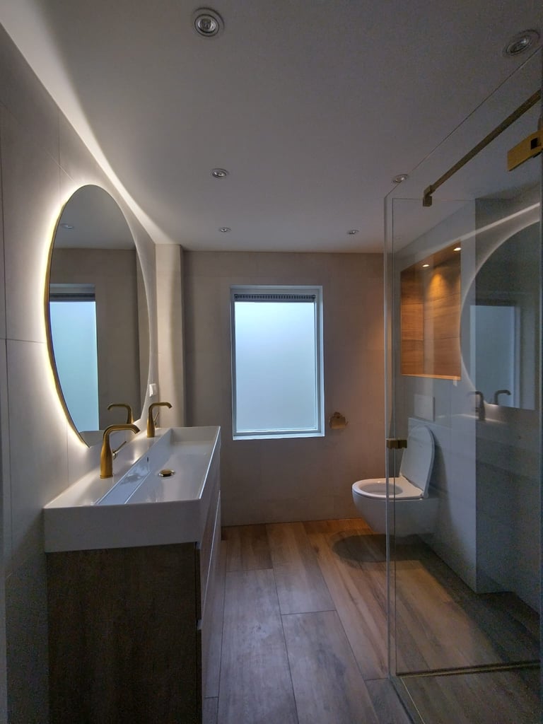 Moderne badkamer met een dubbele wastafel, daarboven een grote spiegel. Gouden kranen. Nis met verli