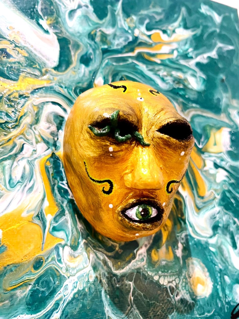 une sculpture sans yeux avec un oeil dans la bouche qui émerge d'une toile verte vu de près