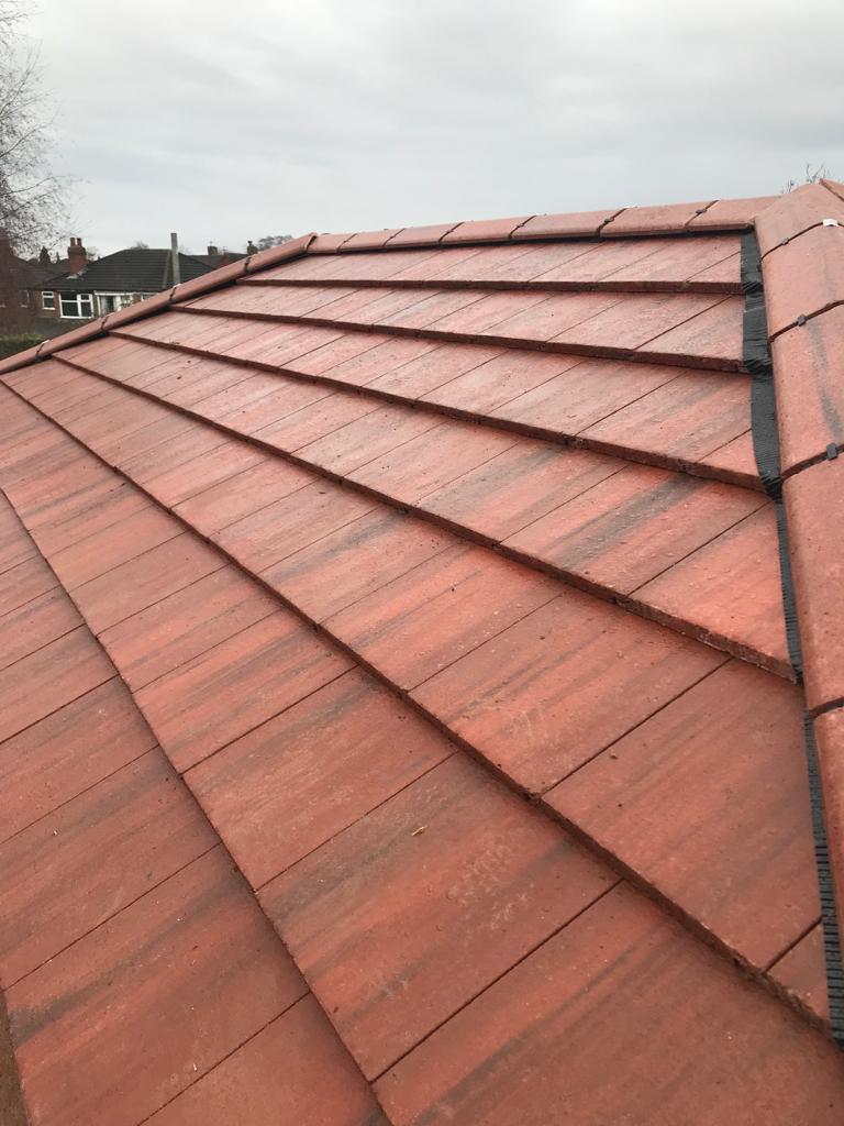 Red interlocking clay roof tiles installed on a residential house hip roof with ridge details.