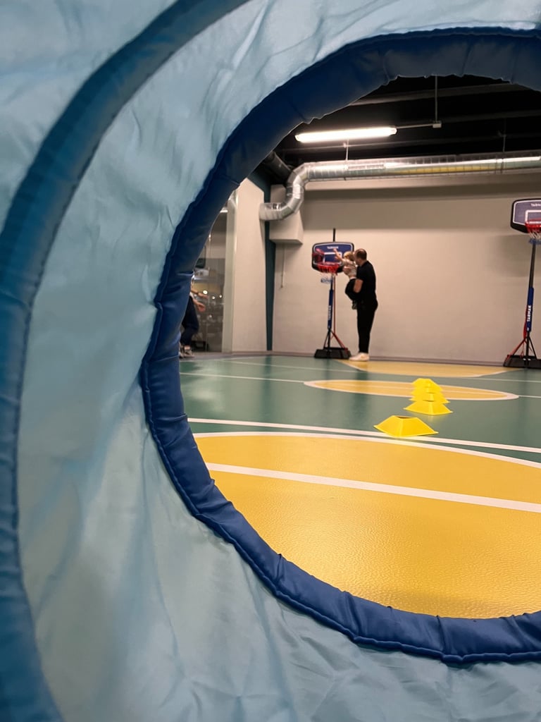 Vista attraverso un tunnel morbido in un'area multisport della palestra Move 2 Grow a Milano, con un adulto che aiuta un bamb