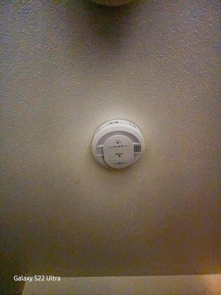 White Kidde smoke detector mounted on a textured ceiling for residential fire safety.