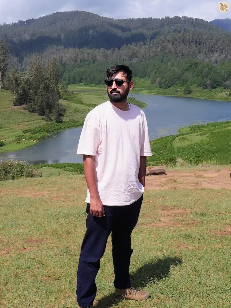 Traveler at Mannavanur Sheep Farm with heart-shaped Mannavanur Lake in the background.