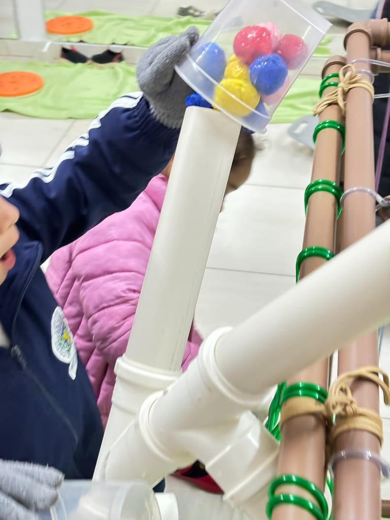 Criança brincado com bolinhas coloridas em canos.