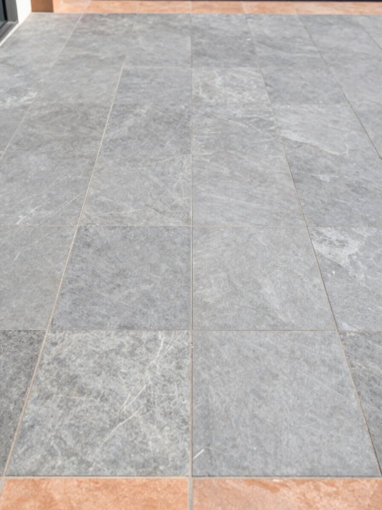 Straight-on architectural elevation of a modern outdoor terrace tiled with large-format slate gray tiles, showcasing flawless alignment and clean drainage integration, bright natural daylight, 35mm