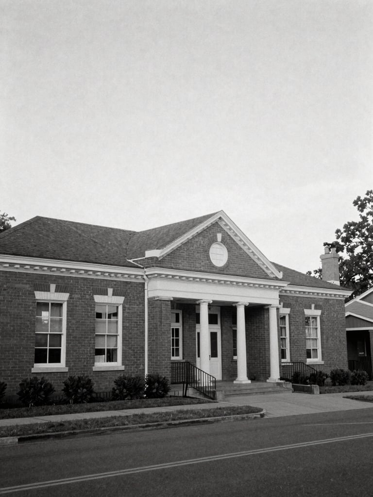 A black and white documentary photograph of a historic brick community center under soft daylight, wide environmental framing, 35mm lens.