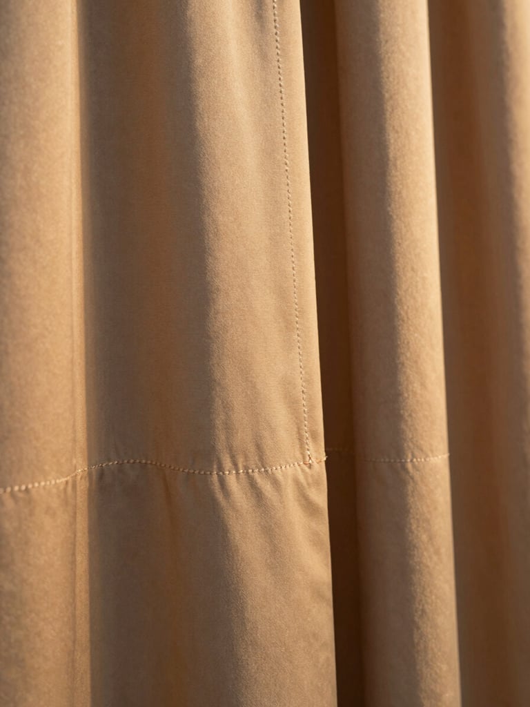 Editorial close-up of a high-quality heavy silk garment hem, warm golden-hour side-light highlighting the precise stitching and premium texture