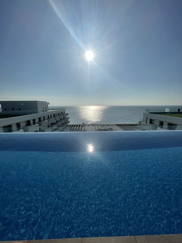 Luxuriöser Infinity-Pool mit Blick auf ein sonniges Strandresort mit Meerblick und strahlendem Sonne
