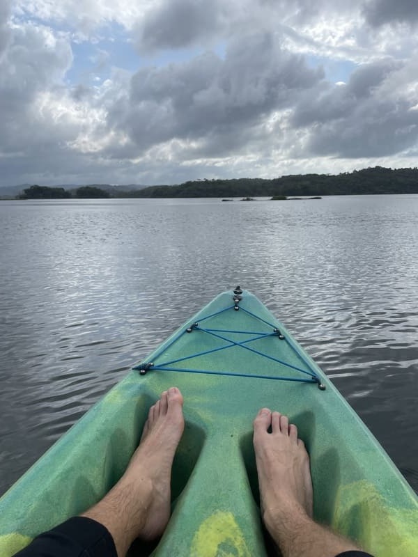 Point-of-View-Aufnahme von Füßen in einem grünen Kajak auf einem ruhigen See unter einem bewölkten