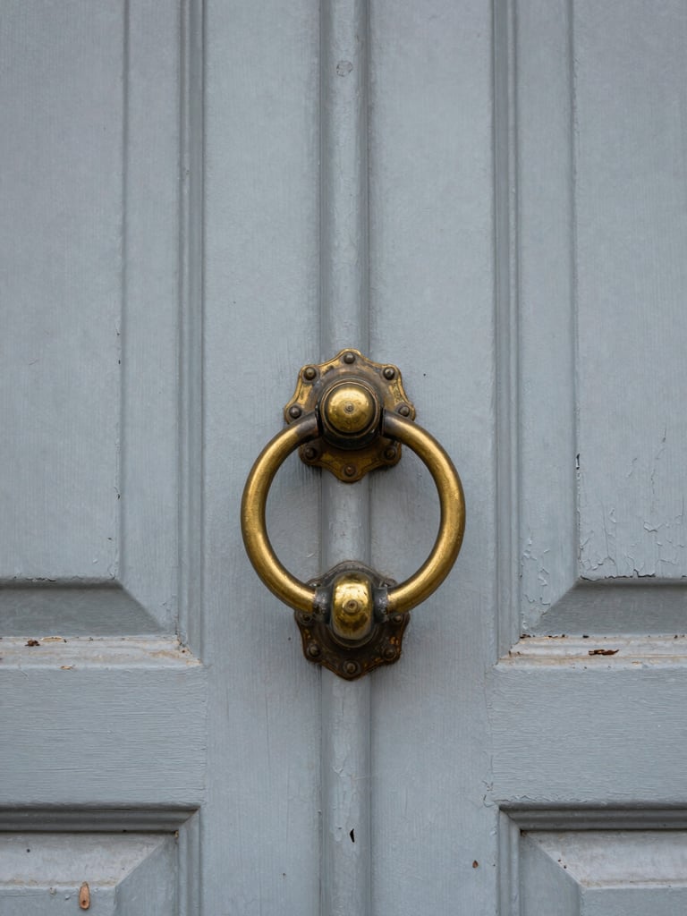 Close documentary shot of a worn front door with peeling paint and a tarnished brass knocker, natural overcast light, honest architectural detail, no staging