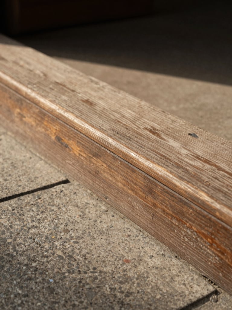 Close-up of a weathered wooden threshold and stone doorstep bathed in soft noon light, worn surface texture visible, no people, warm diffused shadows, eye-level framing with generous negative space to the left