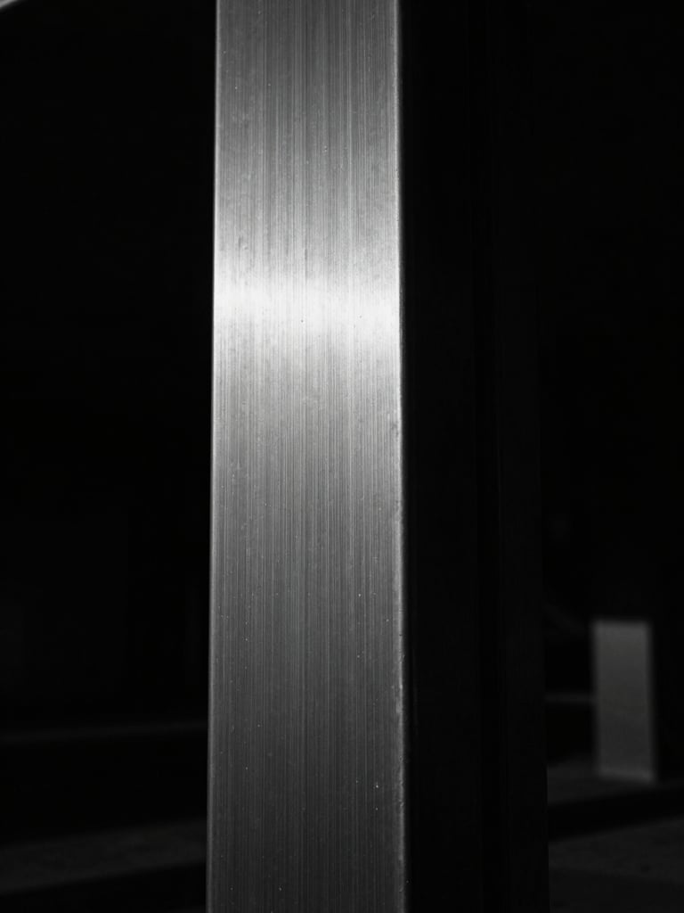 Extreme close-up of a heavy brushed steel structural column, dramatic chiaroscuro lighting, deep shadows, sharp focus, 35mm