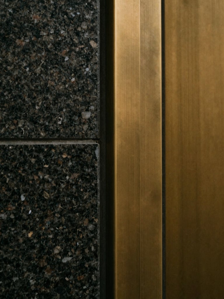 Minimalist close-up of high-quality dark granite and brushed brass materials, soft warm light reflecting off clean edges, architectural detail, 35mm film.
