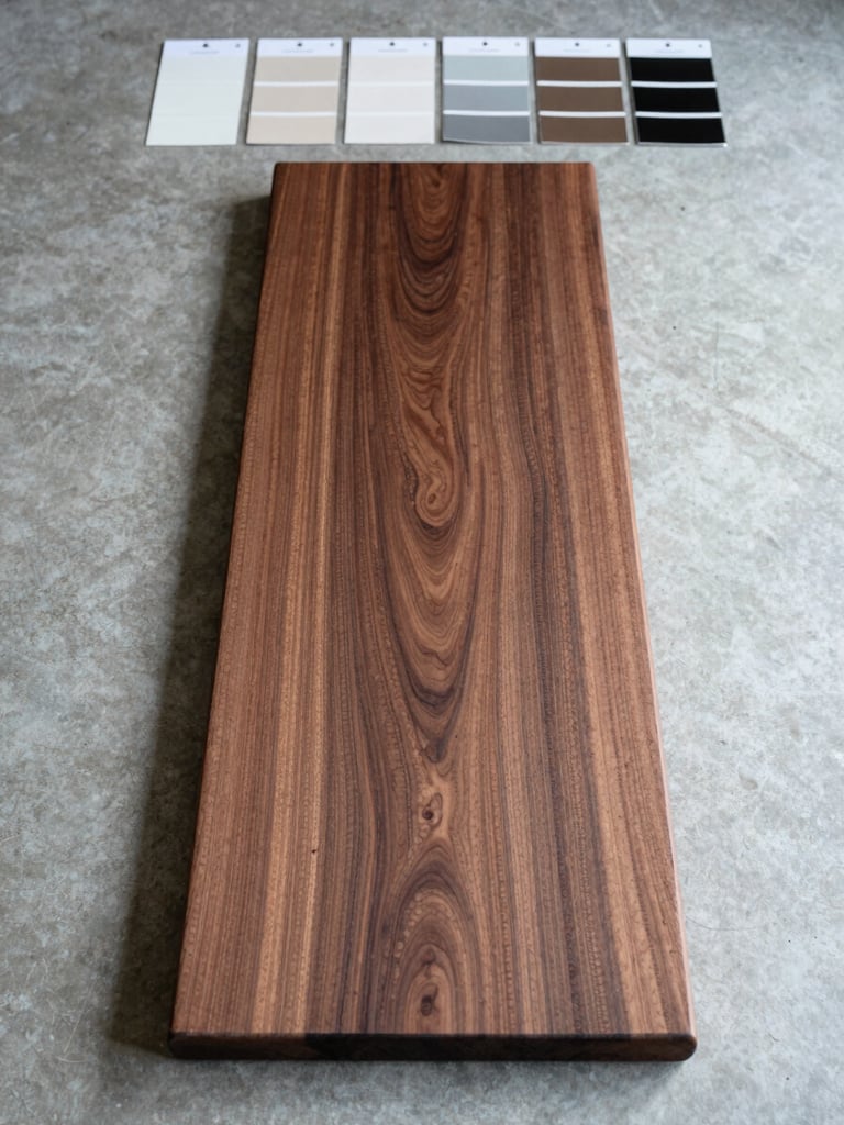 Overhead shot of a full-length walnut board laid flat on a pale concrete surface under cool north-facing daylight, finish sample swatches arranged at the top edge in a precise row, no hands, material documentation aesthetic