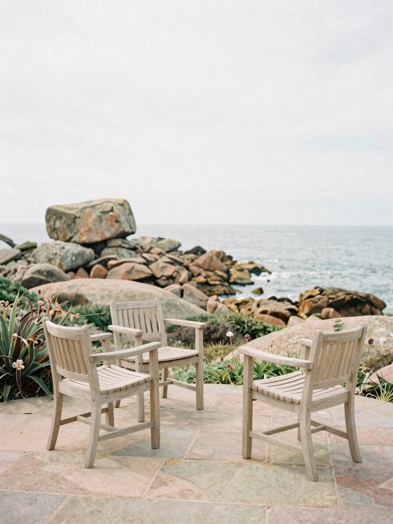 A quiet stone terrace with light wooden chairs, overlooking a wild coastal garden with pink granite rocks and sea views, soft overcast Breton daylight, warm editorial photography, medium format film
