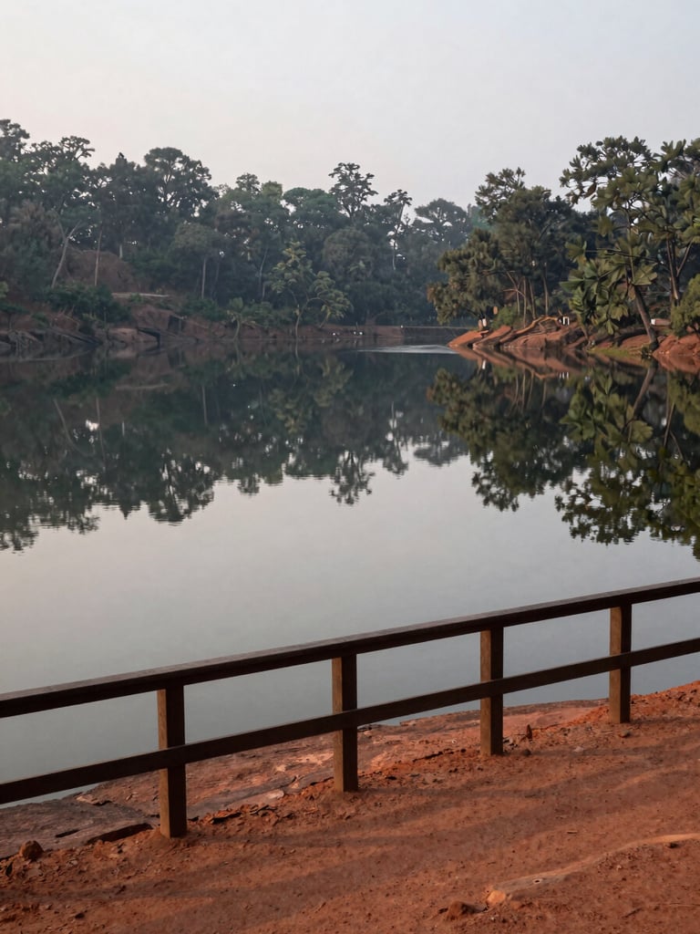 Environmental wide shot of Matheran's Charlotte Lake viewpoint at 7am, overcast diffuse light, still water reflecting treeline, empty wooden railing in foreground, no tourists, red laterite soil path visible to one side
