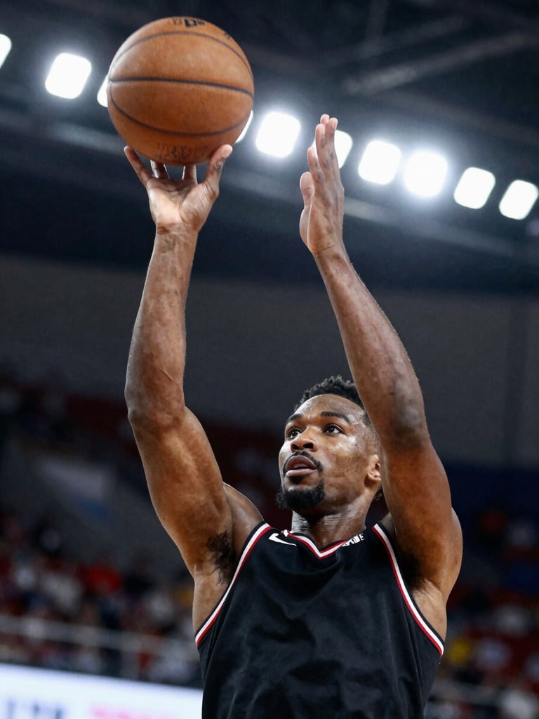 Close-up cinematic frame, African basketball player in mid-air executing a jump shot under bright stadium floodlights, ball at apex of release, court lines visible below, shallow background blur, broadcast-grade sports photography with high contrast