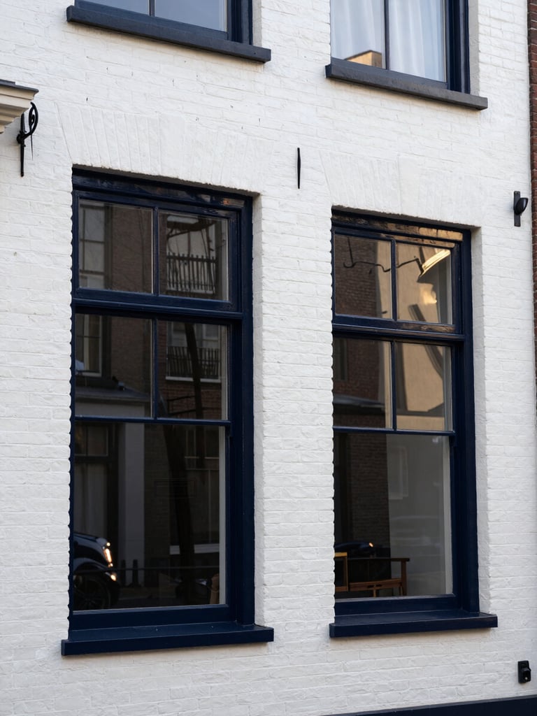 A beautifully restored historic white brick residential facade in Den Haag with glossy dark navy painted window frames reflecting the morning sun, clean lines