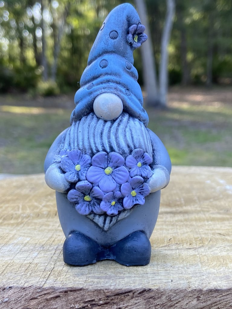A concrete garden gnome figurine holding a bouquet flowers.