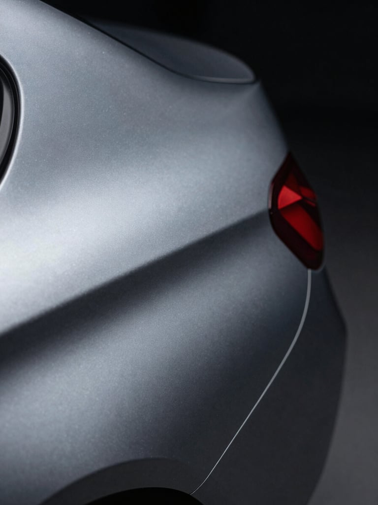 Extreme close-up 2–3 cm macro of a matte-to-metallic vinyl wrap edge transition on a BMW door panel, cool studio side lighting revealing surface texture depth and a perfectly flush seam, dark background, no glare