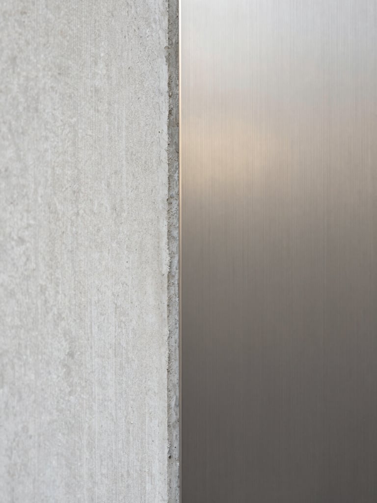 Extreme close-up of raw textured concrete meeting smooth brushed steel, soft diffused side daylight, neutral muted tones, architectural detail study