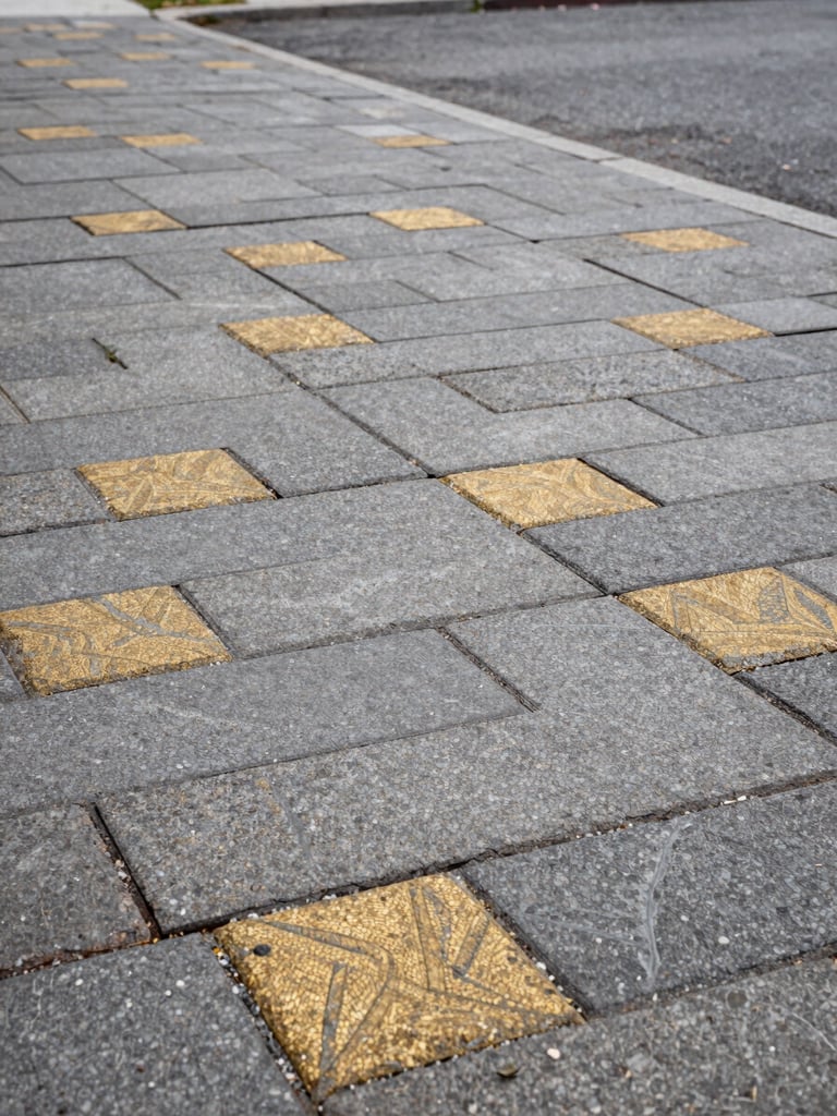 Close-up wide shot of freshly laid interlocking stone paving on a Montreal residential driveway, overcast daylight revealing precise joint lines and rich grey-gold stone texture, camera low and angled to show the material surface stretching to the left edge