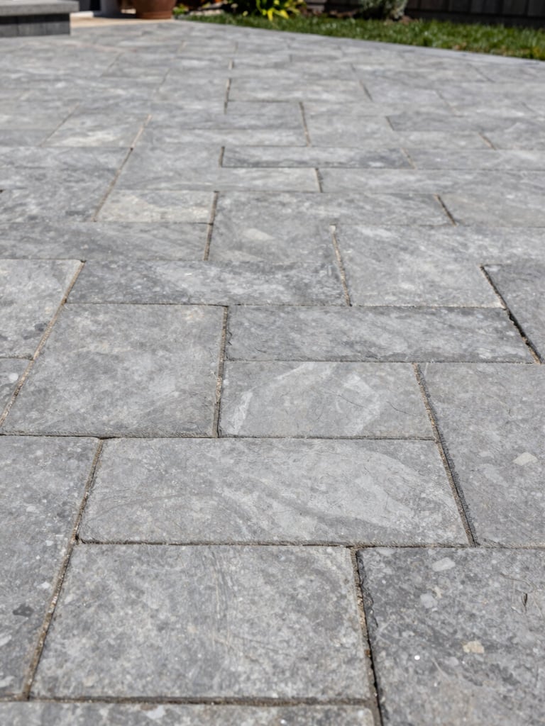 Detailed shot of premium interlocking stone patio installation, uniform joint lines and tight stone-to-stone contact, residential Montreal backyard, natural daylight from above, no people