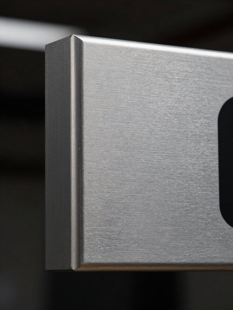 Extreme close-up of a fabricated aluminum sign edge under flat studio lighting, crisp beveled corner and brushed metal surface texture visible in sharp detail, dark background