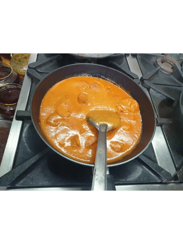 Authentic butter chicken curry simmering in a black frying pan on a gas stovetop.