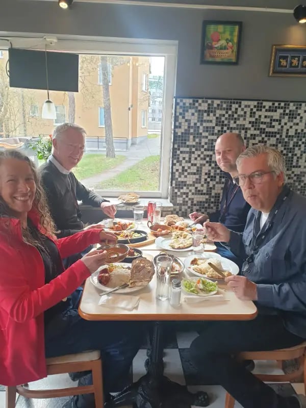 Fyra personer njuter av traditionell indisk mat vid ett restaurangbord med naanbröd och curry.