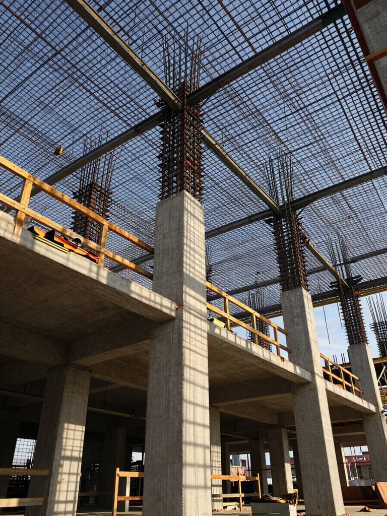 Wide-angle view from below looking up through structural steel formwork and rebar grid on a major construction site, late afternoon natural daylight casting hard geometric shadows through the lattice, raw concrete columns rising beyond the frame, no people